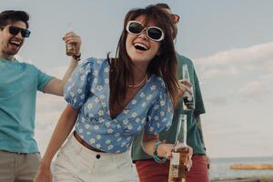 Group of happy friends enjoying beer and dancing while having fun on the beach together photo
