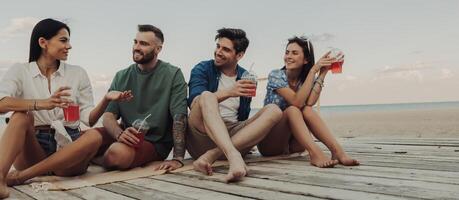 Four young friends enjoying summer cocktails while spending time on the beach together photo