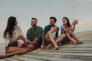 Group of young people talking and smiling while enjoying refreshing cocktails on the beach together photo