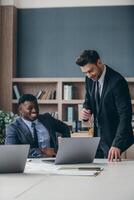 Two happy businessmen in formalwear using computer while working in the office together photo