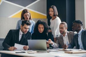 Group of confident young business people looking at laptop while working at the modern office together photo