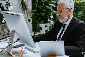 Confident mature man in formalwear using technologies while working in the modern office photo