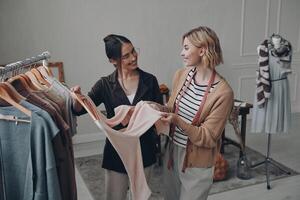 Two happy female fashion designers examining clothes while working in workshop photo