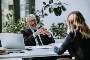 Happy mature man in formalwear interviewing job candidate while sitting at the desk in office photo