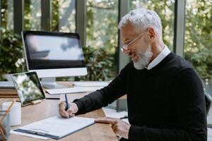 Mature man in smart casual wear signing documents while working with papers in the modern office photo