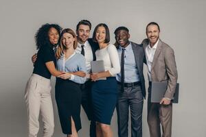 Smiling young business team in formalwear embracing while standing on beige background photo