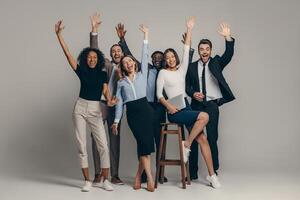 Joyful young business team in formalwear gesturing while standing on beige background photo