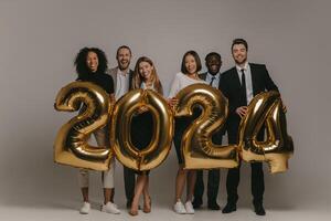 Group of happy business people in formalwear holding 2024 numbers while celebrating New Year on background photo