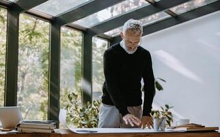 Confident mature architect examining blueprint while working in the creative office photo