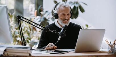 Cheerful mature podcaster in headphones using microphone while broadcasting from studio photo