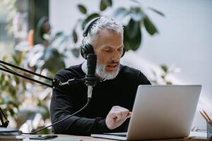 Confident mature presenter recording podcast while looking at computer monitor in studio photo