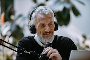 Confident mature presenter in headphones using microphone while recording podcast in studio photo