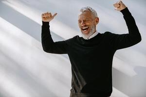 Joyful senior man in smart casual wear looking excited while gesturing against the wall photo