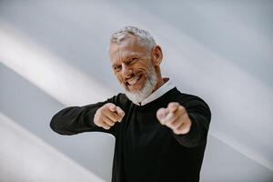 Portrait of happy senior man in smart casual wear gesturing and smiling against the wall photo