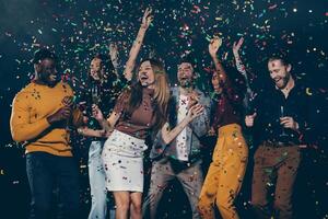 Group of young happy people enjoying champagne and throwing confetti while dancing in night club together photo