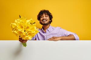 Handsome Indian man stretching out flower bouquet against yellow background photo