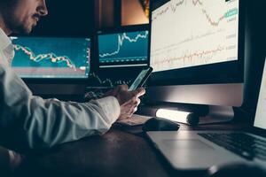Confident male financial broker using technology and analyzing stock market data while working late in office photo
