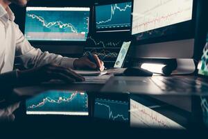 Close-up male trader analyzing stock market data while sitting at the office workstation with multiple computers photo