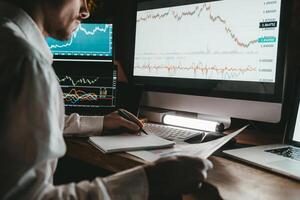 Close-up of male trader analyzing stock market data while using multiple computers in night office photo
