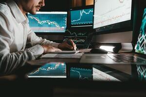 Close-up male trader analyzing stock market data while sitting at the office workstation with multiple computers photo