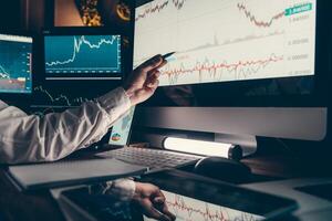 Close-up of male trader pointing computer monitor while analyzing stock market charts in night office photo