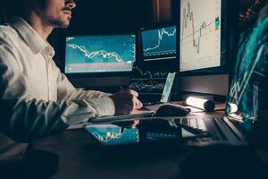 Close-up male trader making notes while analyzing stock market data on multiple computers in night office photo