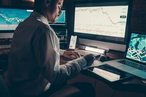 Close-up male trader analyzing stock market data while sitting at the office workstation with multiple computers photo