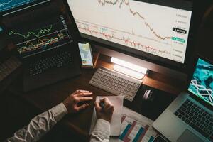 Top view of male trader analyzing stock market data while using multiple computers in night office photo