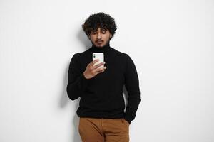 Handsome Indian man using smart phone while standing against background photo