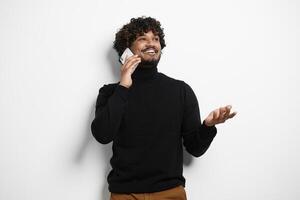 Handsome Indian man talking on phone and smiling while standing against white background photo