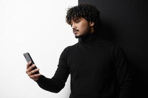 Handsome Indian man using smart phone while standing against black and white background photo