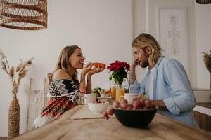 Joyful young loving couple enjoying healthy food and drinks while having breakfast at boho style home photo