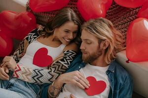 Top view of romantic couple holding heart shape Valentine cards while lying on bed surrounded with red balloons photo