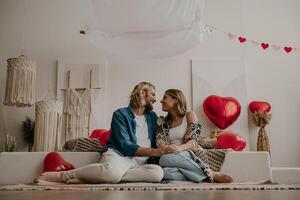 Romantic loving couple holding hands and leaning on bed with red heart shape balloons on background photo