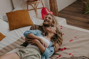 Happy loving couple embracing and having fun while lying in bed surrounded with red heart shape balloons photo