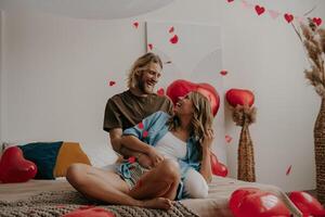 Joyful loving couple sitting on bed and throwing heart shape confetti while celebrating Valentines day at home photo