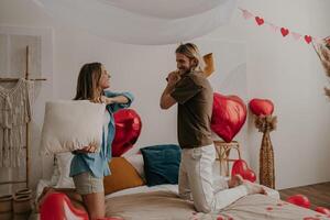 Playful loving couple having a pillow fight in bed surrounded with red heart shape balloons photo