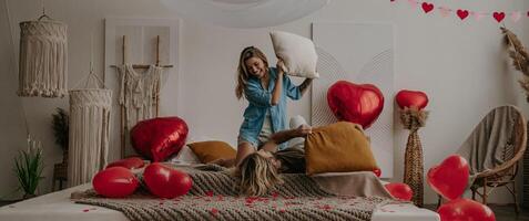 Happy young loving couple having a pillow fight in bed surrounded with red heart shape balloons photo