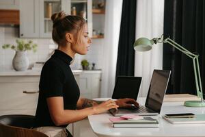 Side view of confident young woman sitting at the desk and using laptop while working at home photo