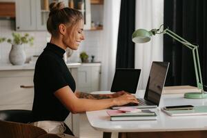 Side view of smiling young woman sitting at the desk and using laptop while working at home photo