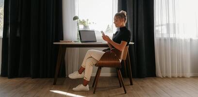 Confident young businesswoman using smart phone while working at home front of the window photo
