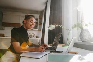 Confident young woman making notes in her note pad and smiling while working at home photo