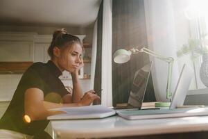 Bored young woman sitting at the desk and looking at laptop while studying at home photo