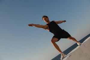 Low angle view of young male athlete doing stretching exercises with the sea view on background photo