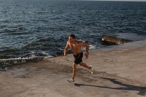 Top view of confident athletic man jogging by the pier with the sea on background photo
