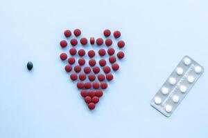 abstract on the topic of a healthy heart, heart disease and the like. bright red pills in the shape of a heart on a bright blue plain background photo