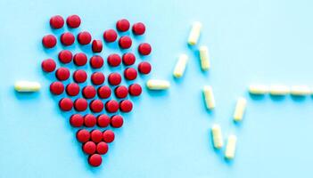abstract on the topic of a healthy heart, heart disease and the like. bright red pills in the shape of a heart on a bright blue plain background photo