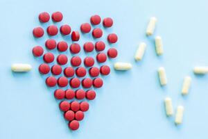 abstract on the topic of a healthy heart, heart disease and the like. bright red pills in the shape of a heart on a bright blue plain background photo
