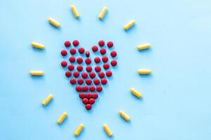 abstract on the topic of a healthy heart, heart disease and the like. bright red pills in the shape of a heart on a bright blue plain background photo