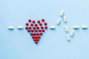 abstract on the topic of a healthy heart, heart disease and the like. bright red pills in the shape of a heart on a bright blue plain background photo